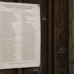 Old parchment with Latin text taped to a dark wooden door, metal studs visible around the edges.