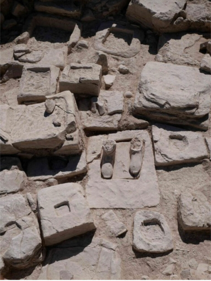 Cipro Pile of weathered stone blocks with rectangular recesses and a few rounded artifacts arranged on dusty ground.