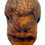 Terracotta head sculpture with closed eyes and a subtle smile, orange-brown with dark markings.