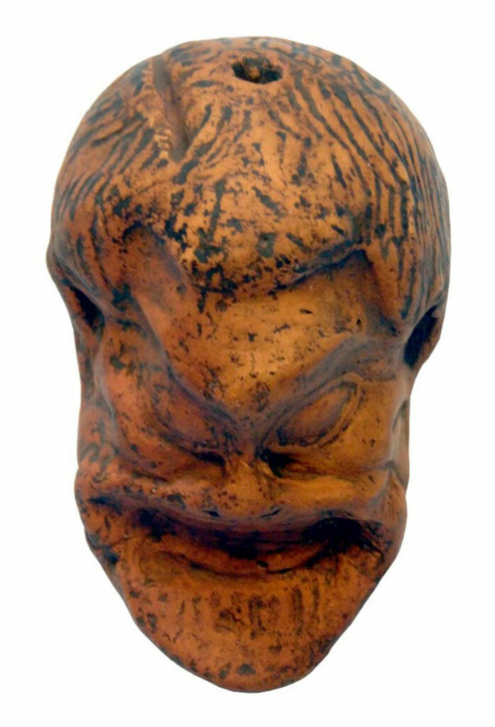 Terracotta head sculpture with closed eyes and a subtle smile, orange-brown with dark markings.