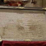 Ornate glass display case with gold trim holding an aged parchment on a red velvet pedestal.
