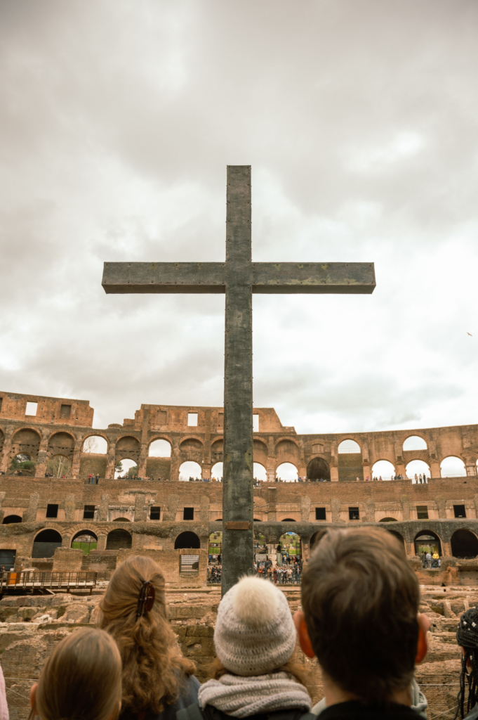 Quello che resta - Scripta Manent Italia Grande croce metallica all'interno del Colosseo di Roma con visitatori che la osservano davanti alle rovine dell'anfiteatro