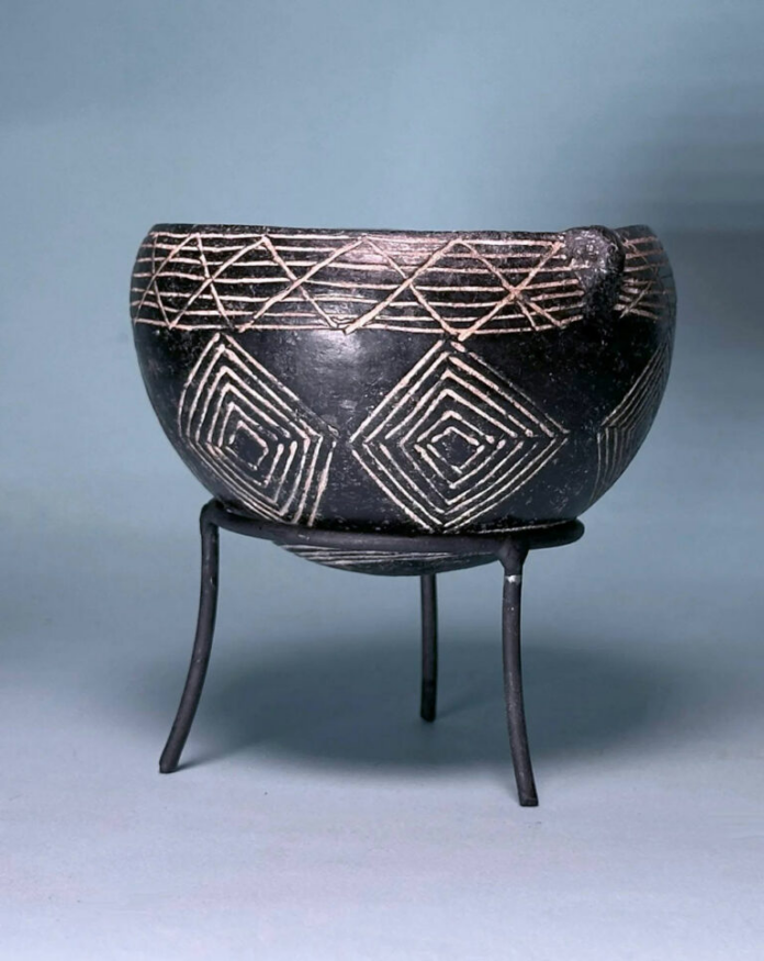 Ciotola Cipro Black ceramic pot with white geometric diamond patterns sits on a three-legged metal stand.