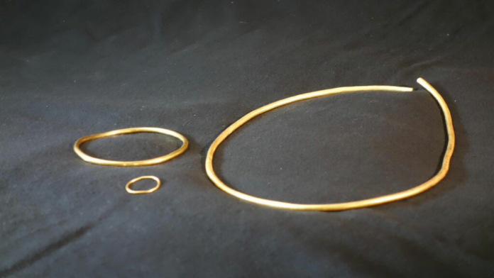 Germany-Gold Three thin gold bangles of varying sizes laid on a dark fabric surface.