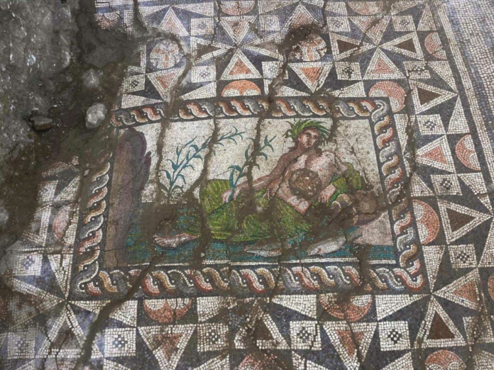 Ancient mosaic floor with a central rectangular panel showing a reclining figure by water, bordered by a twisted rope pattern.