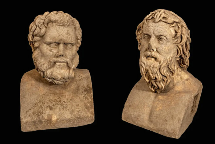 Two weathered stone busts of bearded men on square bases, placed side by side against a black background.
