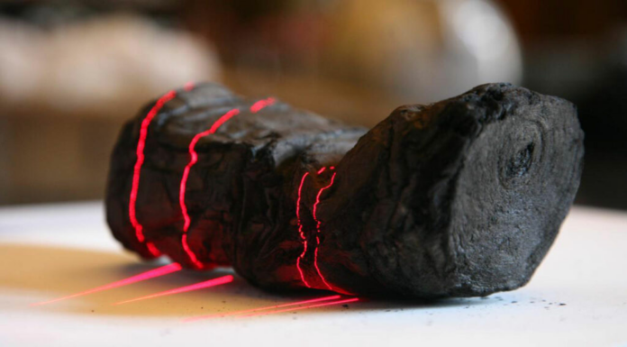 Two black charcoal chunks with glowing red cracks on a white surface, conveying intense heat and energy.