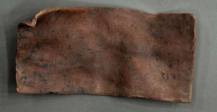 Rectangular piece of worn brown leather with frayed edges and dark stains on a gray background.