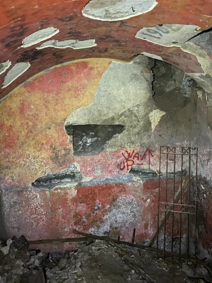 Villa Roma Interior of an abandoned, crumbling room with peeling red paint, exposed plaster, and rubble on the floor.