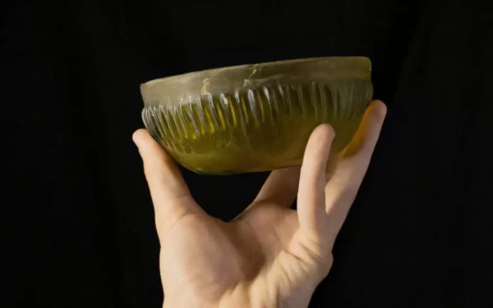 Eta del ferro Hand holding a green ribbed glass bowl against a dark background.