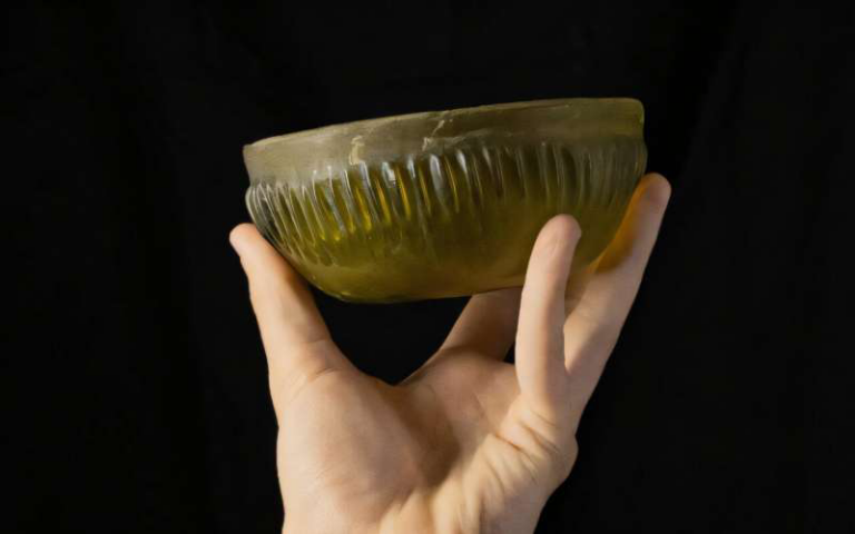 Hand holding a green ribbed glass bowl against a dark background.
