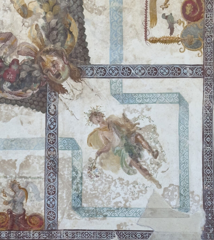 Pompei Faded fresco showing a winged, haloed angel floating within a pale blue-bordered panel, surrounded by ornate geometric frames.