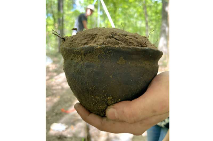 Vaso Close-up of a weathered clay pot filled with soil, held by a hand outdoors in a forest setting.