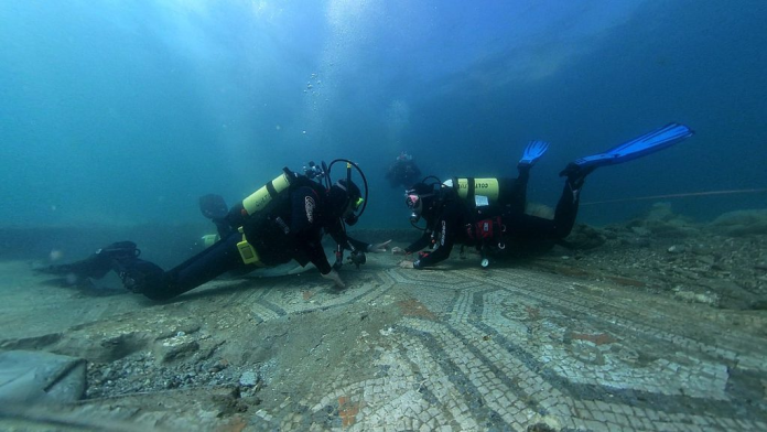 Two scuba divers examine an ancient underwater mosaic on the seafloor.