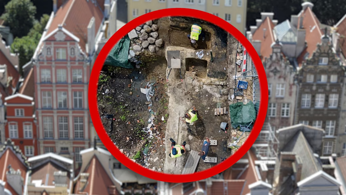 Aerial view of a small construction site circled in red, with workers in safety vests and scattered debris on a city block.