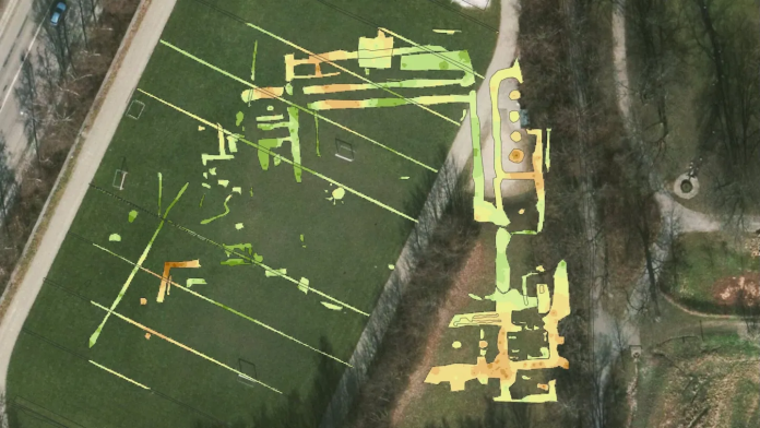 Convento An aerial view of a grassy field with a large lime-yellow map-like overlay and a stone wall along the edge, beside a paved path.