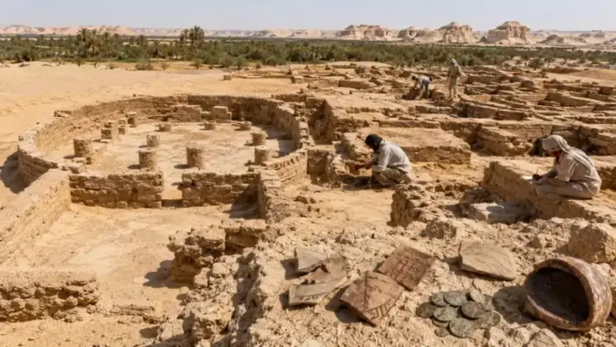Egitto Archaeologists excavating ancient ruins in a desert site, circular stone foundations exposed, with coins and pottery fragments nearby