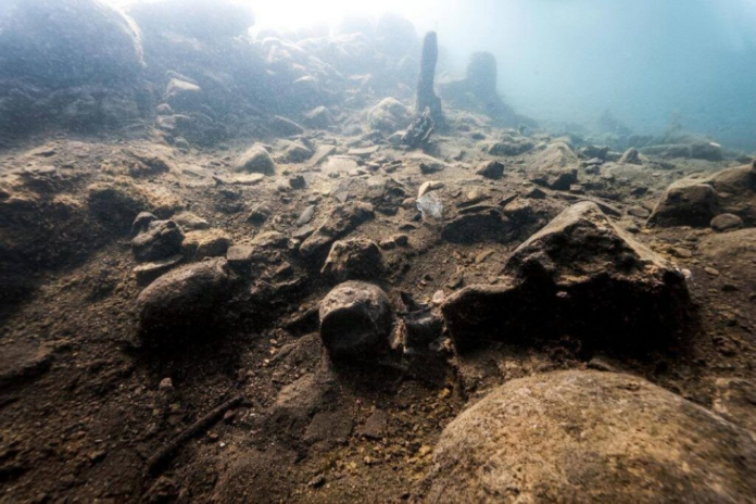 Underwater seabed with numerous rocks and pebbles on a sandy floor, light coming from above