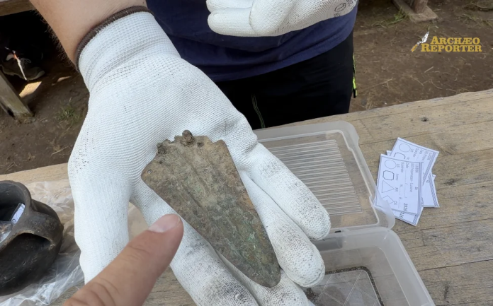 Punta Gloved hand holds a corroded metal blade fragment during fieldwork, with a plastic tool tray and papers nearby.