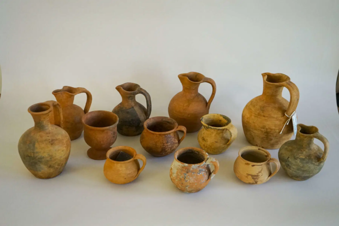 Scoperta Croazia Group of ancient clay vessels and jugs arranged on a white surface, varying in shape and size.