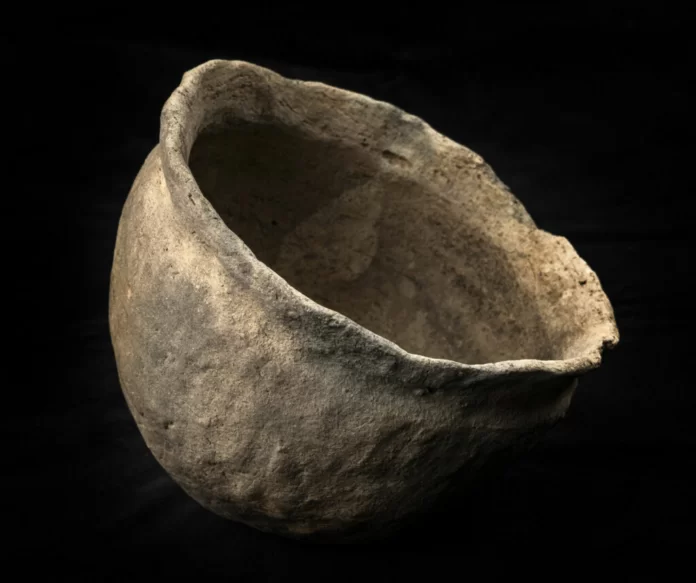 Rough, weathered ceramic bowl fragment resting on a dark background.