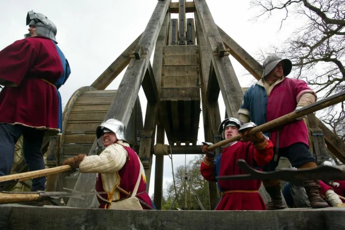 Group of people in medieval costumes operating a large wooden trebuchet during a reenactment event.