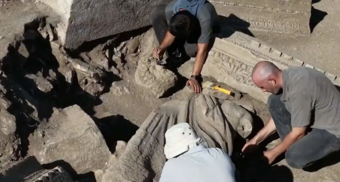 turchia-aspendo-gruppo-marmoreo-romano Archaeologists carefully excavating around a carved stone relief partially buried in dirt.