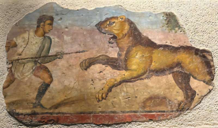 Fragment of an ancient wall painting showing a man chasing a large snarling dog with a spear bedded on a rough plaster wall.