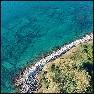 Pozzuoli Aerial view of a curved rocky breakwater along a turquoise coastline with green vegetation onshore.