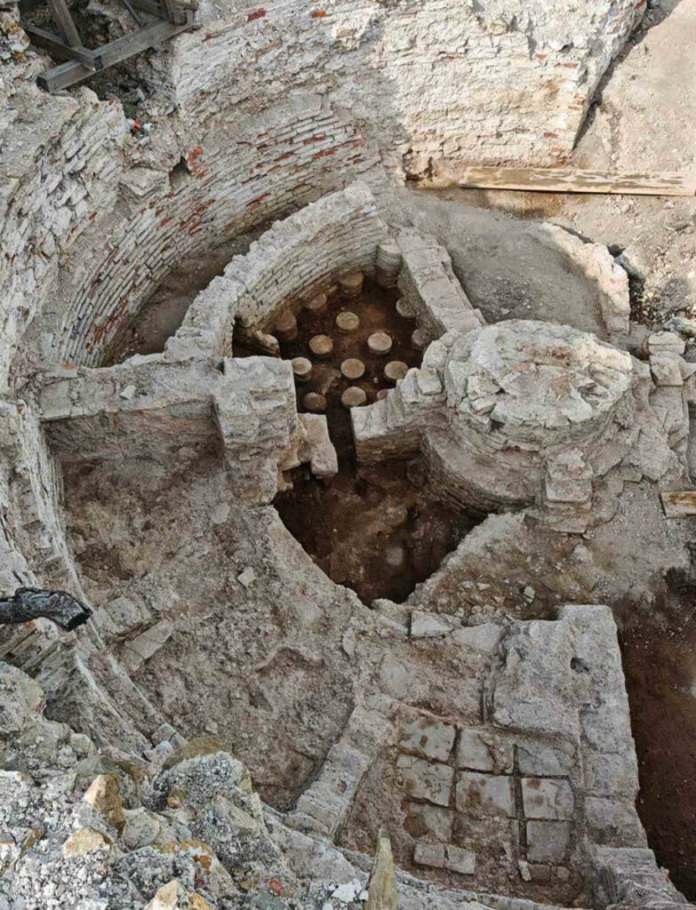 Archaeological dig: circular stone chamber with brick-lined walls and an internal rhythm of stone blocks at the center of excavation site