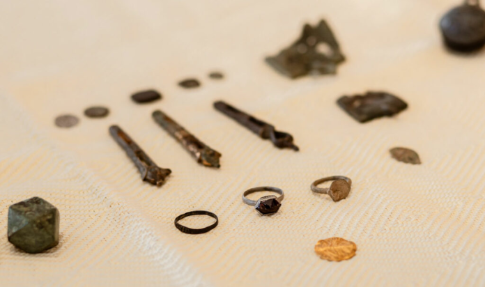 Assorted jewelry pieces and rough minerals laid out on beige fabric, including rings and a dark gemstone