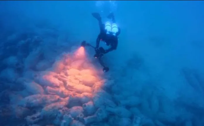 Lipari SCUBA diver underwater shining a flashlight on a rocky seabed with soft coral, blue water surrounding them